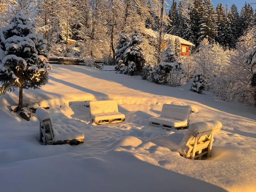 Verschneiter Garten im Abendlicht, die Sitzbänke an der Feuerstelle unter Schnee