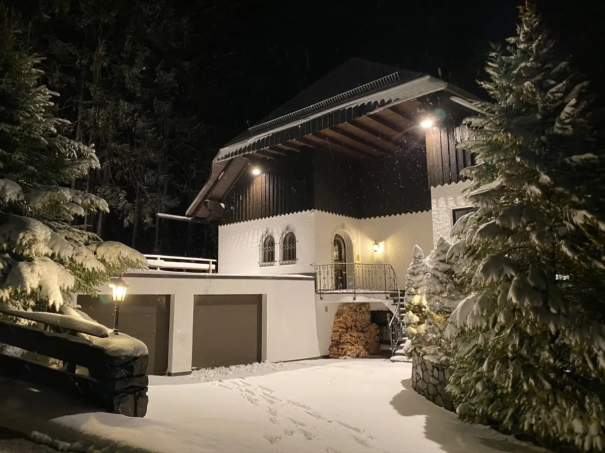 Vorderseite der Villa mit beiden Garagen in einer Schneenacht, Fenster beleuchtet